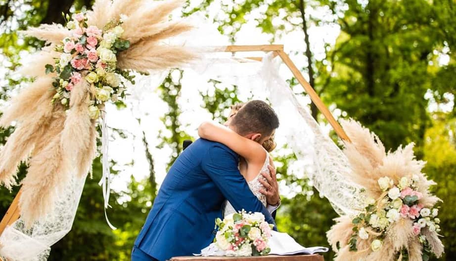 Des mariés s'enlaçant avec une arche de fleurs